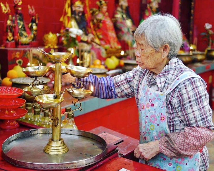 Old wrinkled chinese lady lighting incense sticks at the Tin Hau temple in Stanley. 